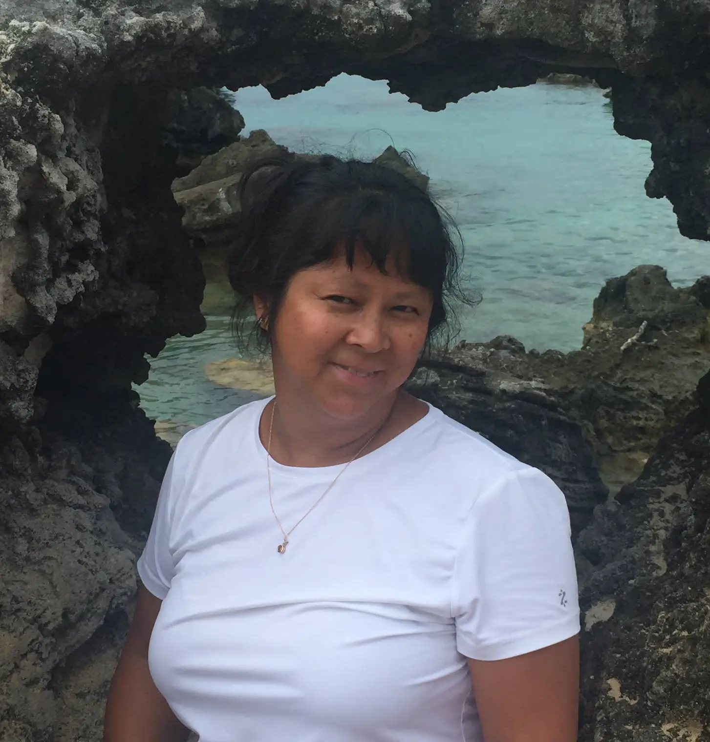 Charlene Gotschall in a white t-shirt posing adorably by a rocky shore.